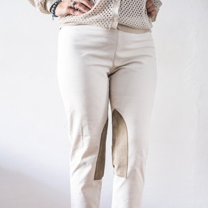 Puede incluir: Pantalón de montar blanco con parches de gamuza marrón en las rodillas. El pantalón es corto y tiene un ajuste delgado. La modelo lleva zapatos de tacón marrón.