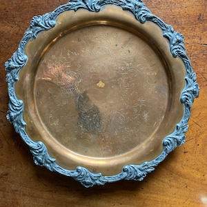 Könnte beinhalten: Ein Vintage-Serviertablett aus Messing mit einem verzierten, silberfarbenen Filigranrand. Die Oberfläche des Tabletts hat einen warmen, goldenen Farbton und weist ein geätztes Blumendesign auf. Der dekorative Rand verleiht dem Stück einen Hauch von Eleganz.