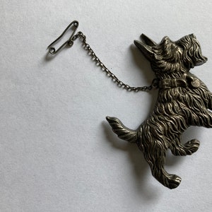 May include: A silver-toned brooch of a Scottish terrier dog with a chain and safety pin.
