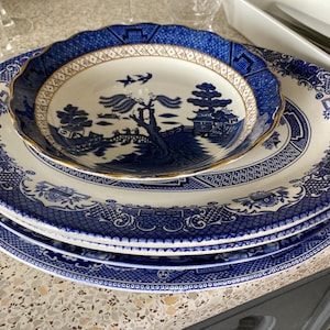 Może przedstawiać: Zestaw trzech niebiesko-białych talerzy porcelanowych z tradycyjnym wzorem wierzby. Talerze są ułożone jeden na drugim, a najmniejszy talerz znajduje się na górze.