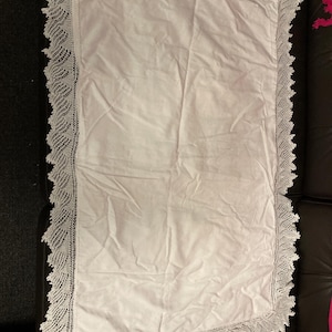 May include: A white rectangular blanket with a delicate, scalloped lace border. The blanket is made of a soft, possibly cotton, fabric. The lace trim adds a touch of elegance to the simple design. The blanket is likely for a bed or a decorative throw.