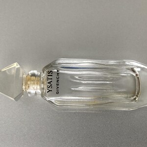 May include: A clear glass perfume bottle with a geometric stopper. The bottle is rectangular with a curved top and features the text "YSATIS GIVENCHY". The stopper is a clear, faceted shape.