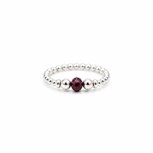 May include: A stretch ring composed of small, polished silver-toned spherical beads arranged in a continuous band. The centre of the ring features a single, faceted, deep red gemstone bead flanked by two larger, smooth, polished silver-toned beads.