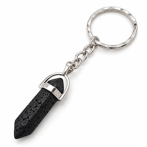 May include: A keyring featuring a black, porous, hexagonal-shaped lava stone pendant suspended from a silver-toned metal cap. The pendant is attached to a silver-toned chain and a circular, textured metal split ring for securing keys.