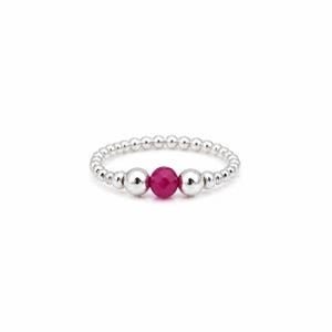 May include: A stretch ring composed of small, polished silver-toned beads arranged in a continuous circular band. The center of the ring features a single, faceted, vibrant pink bead flanked by two smooth, round, silver-toned metallic beads.