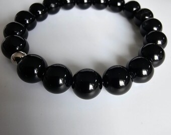 May include: A black beaded bracelet featuring large, round beads with a glossy finish. The beads are strung together with a silver-coloured clasp. The bracelet is presented on a white surface.