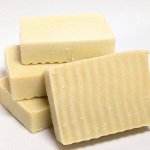 May include: A stack of four rectangular bars of off-white soap. The bars have a smooth, solid appearance with a subtle wavy, ridged texture on the front-facing surface of the foremost bar, while the other bars appear smooth and flat.
