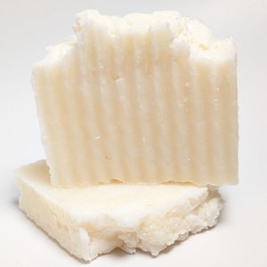 Pu&ograve; includere: Una saponetta rettangolare color bianco sporco con una superficie testurizzata e scanalata sul lato anteriore. Il sapone &egrave; posizionato in verticale, appoggiato su un secondo pezzo pi&ugrave; piatto dello stesso sapone, con una consistenza opaca e irregolare.