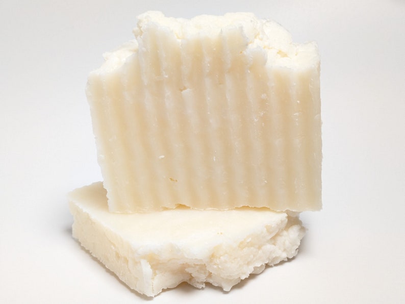 Pu&ograve; includere: Una saponetta rettangolare color bianco sporco con una superficie testurizzata e scanalata sul lato anteriore. Il sapone &egrave; posizionato in verticale, appoggiato su un secondo pezzo pi&ugrave; piatto dello stesso sapone, con una consistenza opaca e irregolare.