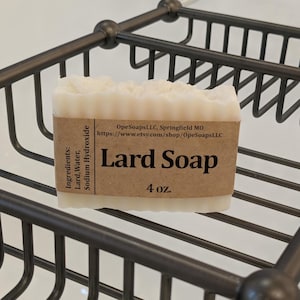 Pu&ograve; includere: Una saponetta rettangolare di colore bianco a base di strutto con il bordo superiore testurizzato. Un'etichetta di carta marrone avvolge il centro, stampata con il testo Lard Soap, 4 oz., OpeSoapsLLC, Springfield MO, e un elenco di ingredienti tra cui Lard, Water, Sodium Hydroxide.