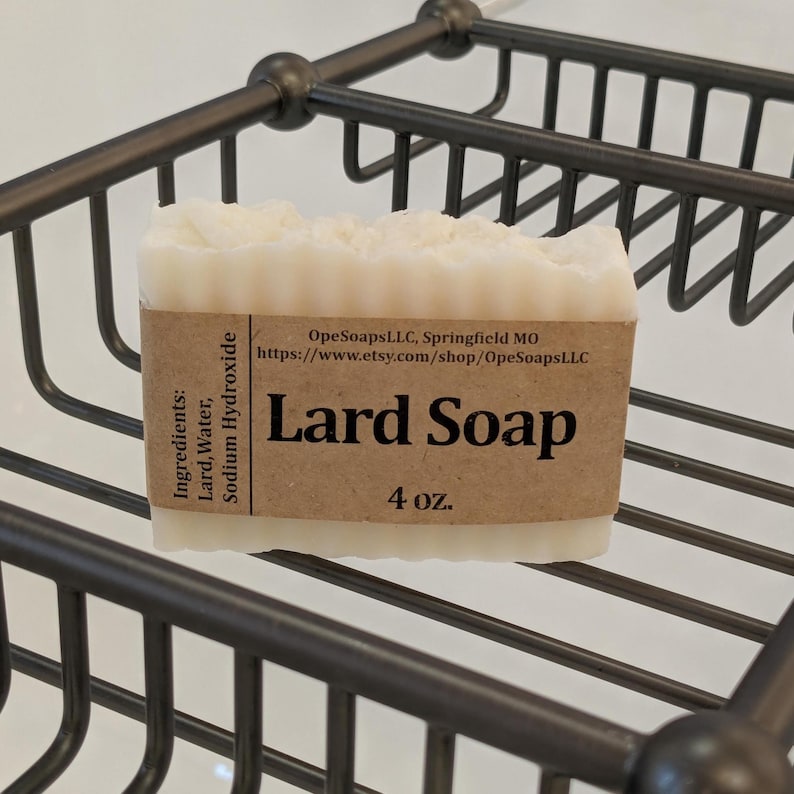 Pu&ograve; includere: Una saponetta rettangolare di colore bianco a base di strutto con il bordo superiore testurizzato. Un'etichetta di carta marrone avvolge il centro, stampata con il testo Lard Soap, 4 oz., OpeSoapsLLC, Springfield MO, e un elenco di ingredienti tra cui Lard, Water, Sodium Hydroxide.