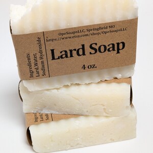 Pu&ograve; includere: Una pila di tre barre rettangolari di sapone allo strutto bianco avvolte in etichette di carta marrone. L'etichetta superiore riporta Lard Soap, 4 oz., OpeSoapsLLC, Springfield MO, ed elenca gli ingredienti Lard, Water, Sodium Hydroxide.