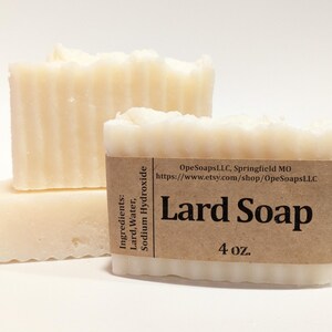 Pu&ograve; includere: Tre barre rettangolari di sapone allo strutto color bianco sporco con una consistenza scanalata. Un'etichetta di carta marrone avvolge la barra anteriore, stampata con il testo Lard Soap, 4 oz., ingredienti e l'URL del negozio OpeSoapsLLC, Springfield MO.