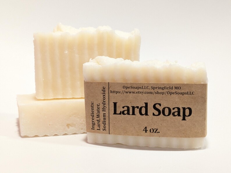 Pu&ograve; includere: Tre barre rettangolari di sapone allo strutto color bianco sporco con una consistenza scanalata. Un'etichetta di carta marrone avvolge la barra anteriore, stampata con il testo Lard Soap, 4 oz., ingredienti e l'URL del negozio OpeSoapsLLC, Springfield MO.