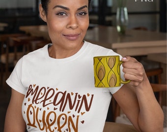 Könnte beinhalten: Eine Frau trägt ein weißes T-Shirt mit dem Schriftzug "Melanin Queen" in brauner Schrift und Herzakzenten. Sie hält einen gelben Becher mit einem braunen geometrischen Muster. Der Becher hat einen gebogenen Griff. Das Bild ist in Innenräumen aufgenommen.