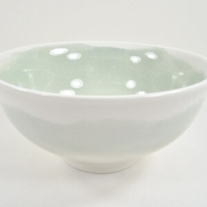 May include: A white ceramic bowl with a pale green interior. The bowl has a rounded shape and a smooth, glossy finish. The interior has a subtle, speckled pattern. The bowl is suitable for serving food.