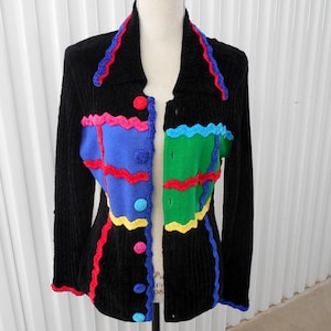 May include: Black cardigan with a colorful geometric pattern on the front. The pattern features red, blue, green, yellow, and pink accents.