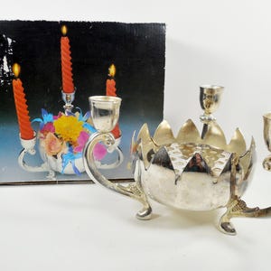 May include: Silver candelabra with three candle holders and a central flower holder. The candelabra has a lotus flower design and is decorated with a floral pattern.
