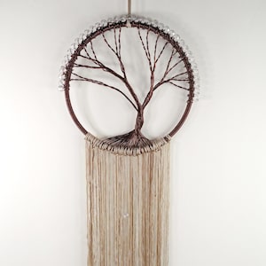 May include: A circular wall hanging featuring a dark brown wire tree sculpture inside a hoop. The upper half of the hoop is adorned with clear beads. A long, beige fiber fringe hangs from the bottom half of the hoop, creating a textured, layered appearance.