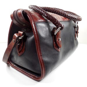 May include: A structured handbag featuring a smooth black leather body contrasted with dark brown crocodile-embossed leather trim. The bag includes two thick, braided dark brown leather handles and a matching detachable shoulder strap with metal hardware.