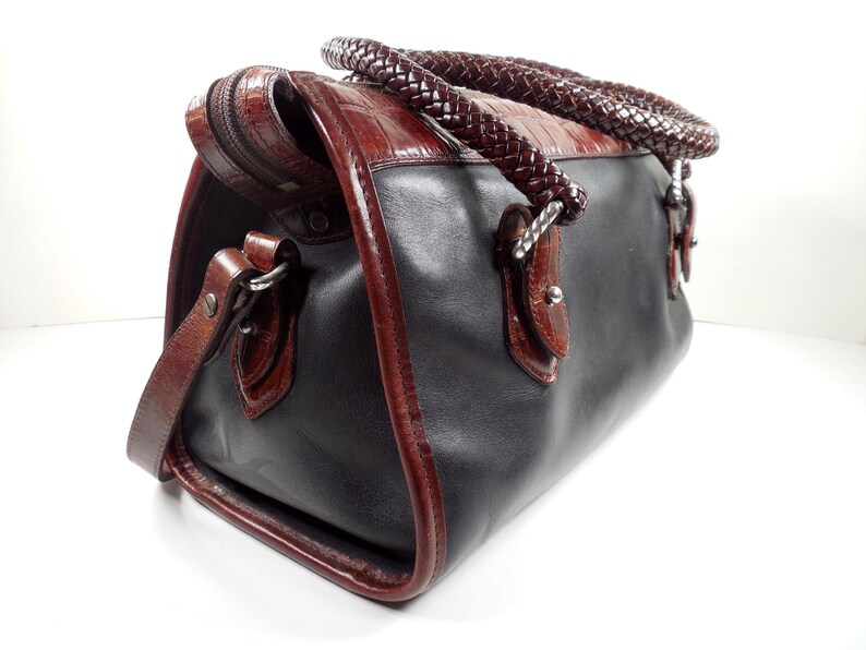May include: A structured handbag featuring a smooth black leather body contrasted with dark brown crocodile-embossed leather trim. The bag includes two thick, braided dark brown leather handles and a matching detachable shoulder strap with metal hardware.