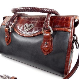 May include: A structured handbag featuring a smooth black leather body contrasted with dark brown crocodile-embossed leather trim. It includes braided leather handles, a silver-toned heart-shaped metal emblem, and a detachable shoulder strap.