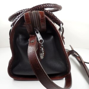 May include: A dark brown handbag featuring a textured crocodile-embossed leather top panel and smooth leather sides. The bag includes a braided leather handle, a top zipper closure with a silver-toned metal pull, and a thin adjustable shoulder strap.