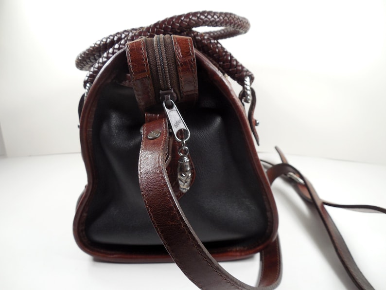 May include: A dark brown handbag featuring a textured crocodile-embossed leather top panel and smooth leather sides. The bag includes a braided leather handle, a top zipper closure with a silver-toned metal pull, and a thin adjustable shoulder strap.