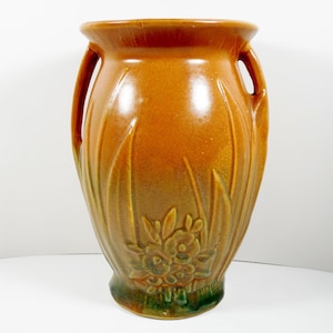 May include: A brown glazed ceramic vase with two handles and a floral design. The vase has a green glaze at the bottom and features a design of stylized flowers and leaves.