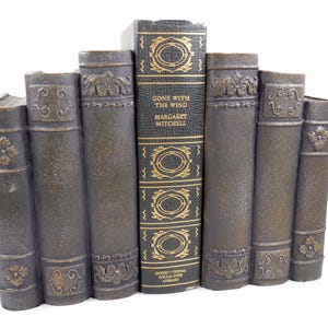 May include: A decorative bookend shaped like a row of antique books. The central book is titled "Gone With The Wind" by Margaret Mitchell. The bookend is primarily dark gray with gold accents and floral and scroll details.
