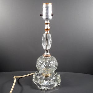 May include: A clear glass table lamp with a square base and a round, textured shade. The lamp has a silver metal socket and a brown cord.
