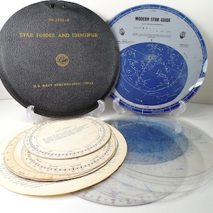 May include: A vintage U.S. Navy Hydrographic Office Star Finder and Identifier set. Includes a black textured circular case, a Modern Star Guide disc with blue celestial maps, and several beige paper discs with printed astronomical data and scales.
