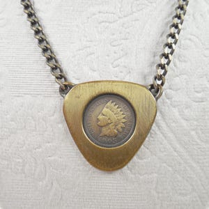 May include: A necklace featuring a triangular brass pendant with a brushed finish, centered with an 1895 United States Indian Head penny. The pendant is attached to a dark metal curb chain that connects to the top corners of the triangular frame.