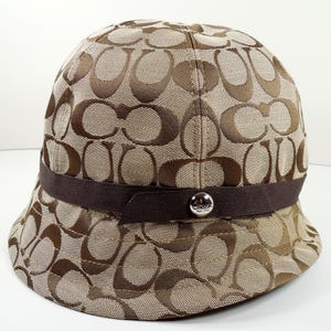 Sombrero de pescador cloche de lona Coach Signature en marrón tostado y beige, talla P/S, pequeño/pequeño, ribete de cinta de grogrén marrón, remache plateado con el logotipo de Coach