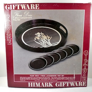 May include: A boxed Fleur Deco 7-piece lacquerware tray set. The set includes a black oval tray with a white floral design and six matching coasters. The box is red with the words "GIFTWARE" and "HIMARK GIFTWARE". The tray is approximately 13.5 inches in diameter.