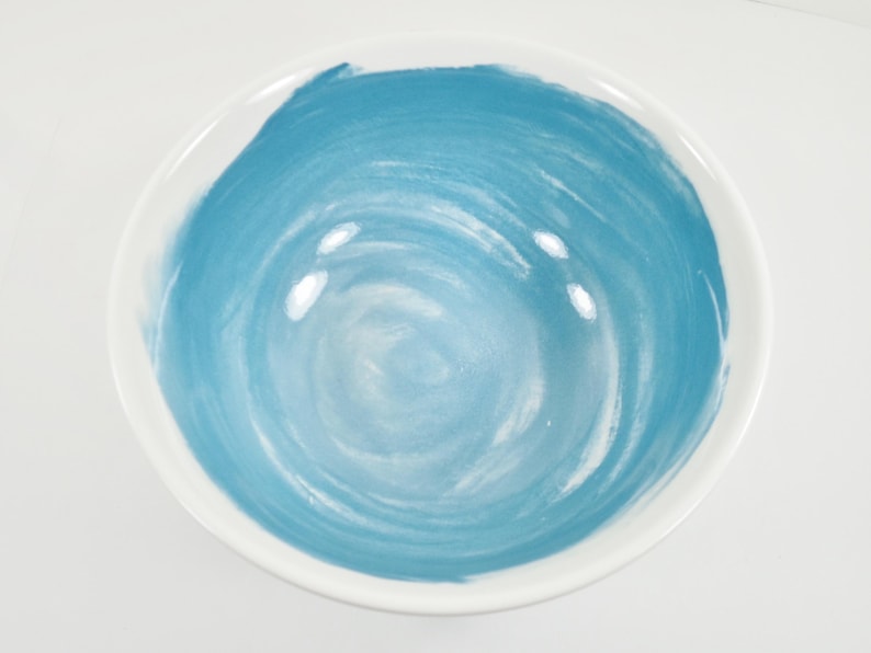 May include: A white ceramic bowl with a hand-painted blue swirl design in the centre. The bowl has a smooth, glossy finish and is suitable for serving food or as a decorative piece.