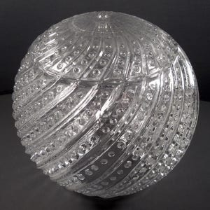 May include: A clear glass lampshade with a textured, swirling pattern. The shade has a round shape and is made of clear glass.