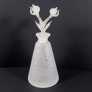 May include: A frosted glass bottle with a floral design and a clear glass stopper with two flower-shaped tops.