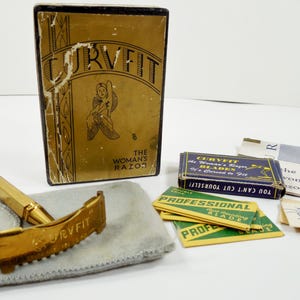 May include: Vintage gold-toned razor set with a box labeled "CURVFIT THE WOMAN'S RAZOR." The set includes a razor, blades, and a small case. The box has a gold finish with an illustration.