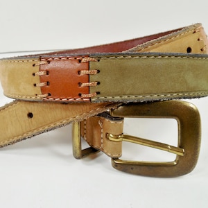 May include: A multi-toned leather belt with a brass buckle. The belt features sections of tan, brown, and olive green leather, stitched together. The buckle is a square shape with a brass finish.