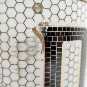 May include: Close-up of a white ceramic mug with a black and gold geometric pattern. The design features a honeycomb pattern and a rectangular mosaic design. The mug has a black handle.