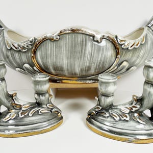May include: A vintage ceramic centerpiece with two matching candle holders. The centerpiece is a gray and white oval-shaped bowl with gold trim. The candle holders are gray and white with gold accents.