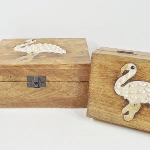 May include: Two wooden boxes with hinged lids, each featuring a white flamingo design inlaid with pearl-like accents. The boxes are made of natural wood with a light brown finish.