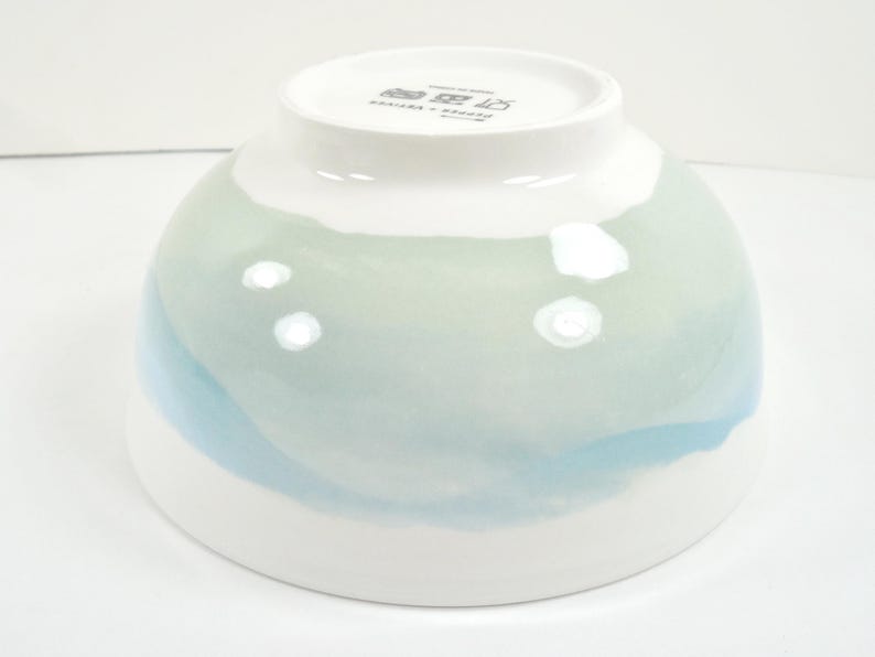 May include: A white ceramic bowl with a rounded shape, featuring a watercolour design in shades of blue and green. The bowl has a glossy finish and a smooth aesthetic, suitable for serving food.
