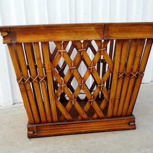 May include: A vintage bamboo magazine rack with a diamond lattice design. The rack is constructed from vertical bamboo poles and features a rectangular shape with a slightly angled front. The bamboo has a warm, natural brown finish.