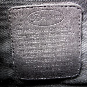 May include: A rectangular black leather patch sewn onto a black fabric lining. The patch features the embossed Brighton logo at the top and text stating that the collection is crafted from quality leathers. The number 550055 is embossed at the bottom.