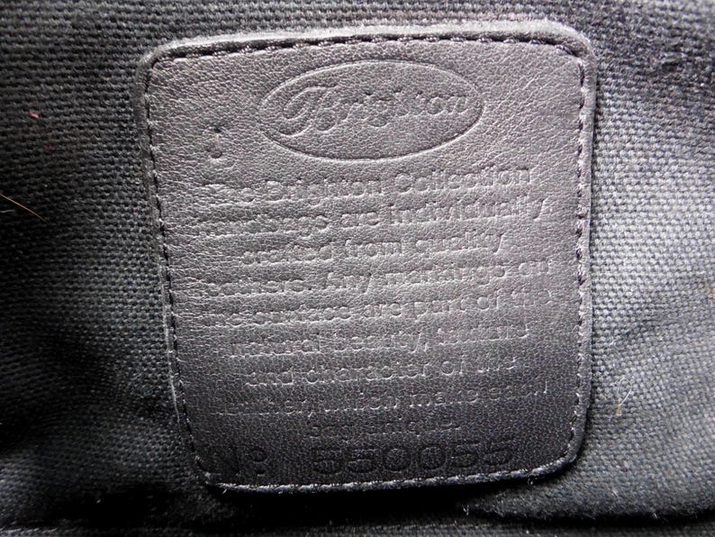 May include: A rectangular black leather patch sewn onto a black fabric lining. The patch features the embossed Brighton logo at the top and text stating that the collection is crafted from quality leathers. The number 550055 is embossed at the bottom.
