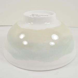 May include: A white ceramic bowl with a rounded shape and a gradient of colours. The bowl transitions from white at the base to a pale green and beige near the top. The bowl has a glossy finish.