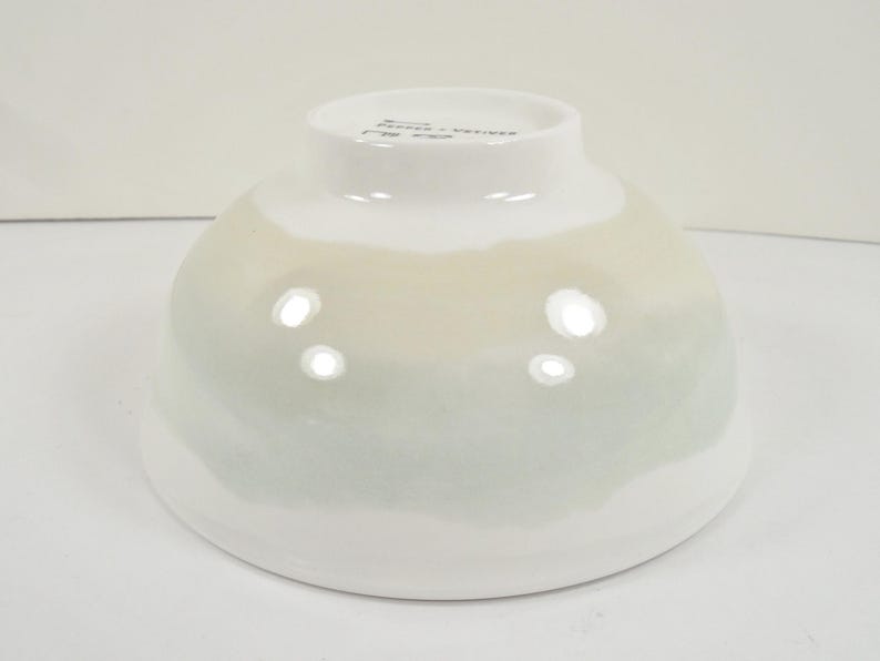 May include: A white ceramic bowl with a rounded shape and a gradient of colours. The bowl transitions from white at the base to a pale green and beige near the top. The bowl has a glossy finish.