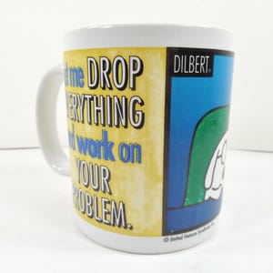 May include: White ceramic mug with a handle, featuring the text "Let me DROP EVERYTHING and work on YOUR PROBLEM." The mug has a yellow background with black and blue text, and a Dilbert cartoon graphic.